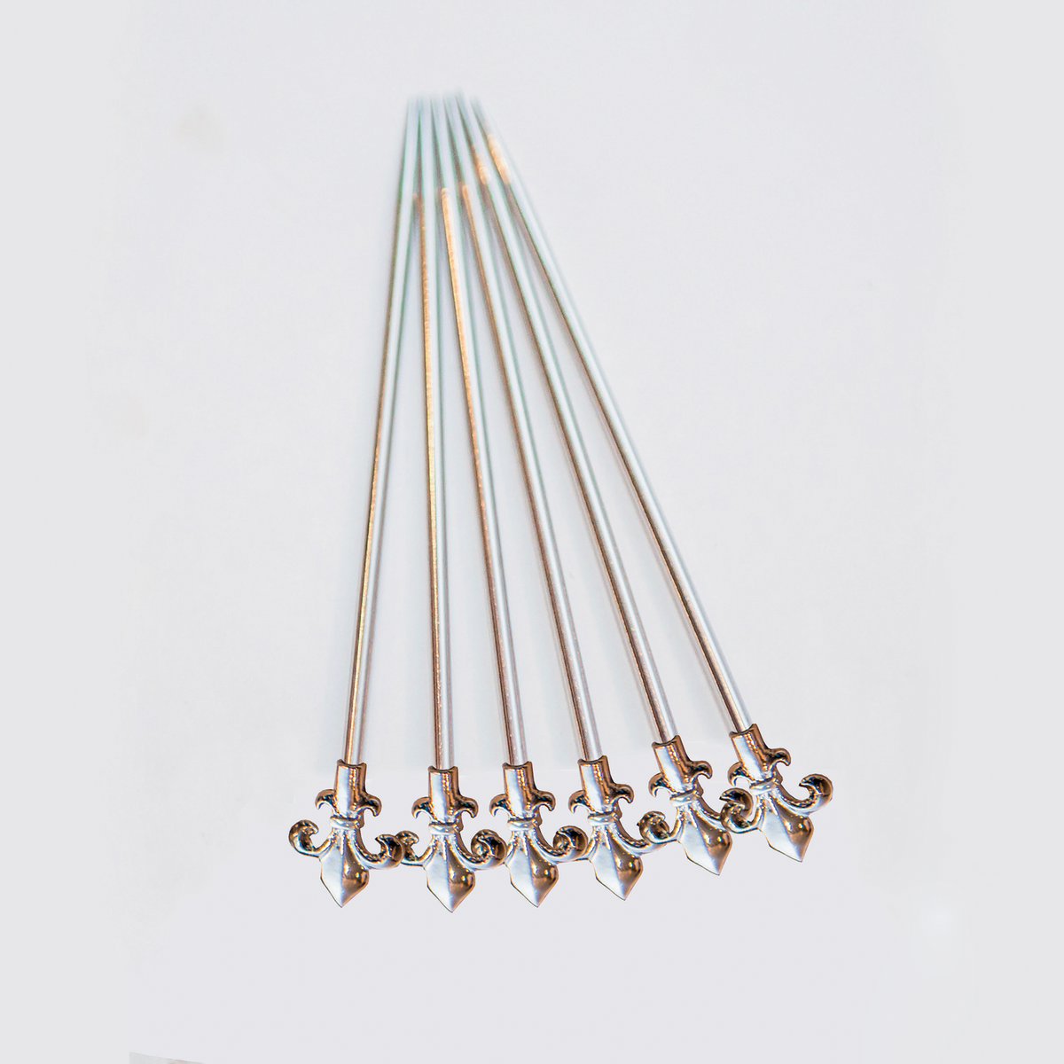 Six stainless steel martini picks with fleur de lys tops, fanned out