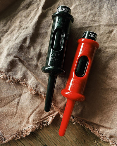 Two Original Cork Pops openers in black and red resting on linen