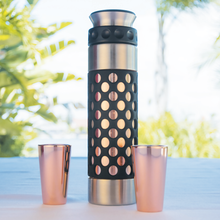 Copper shot glasses beside a matching flask on an outdoor table