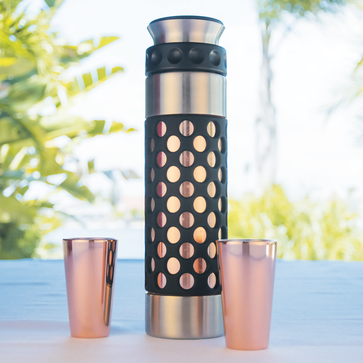 Copper shot glasses beside a matching flask on an outdoor table