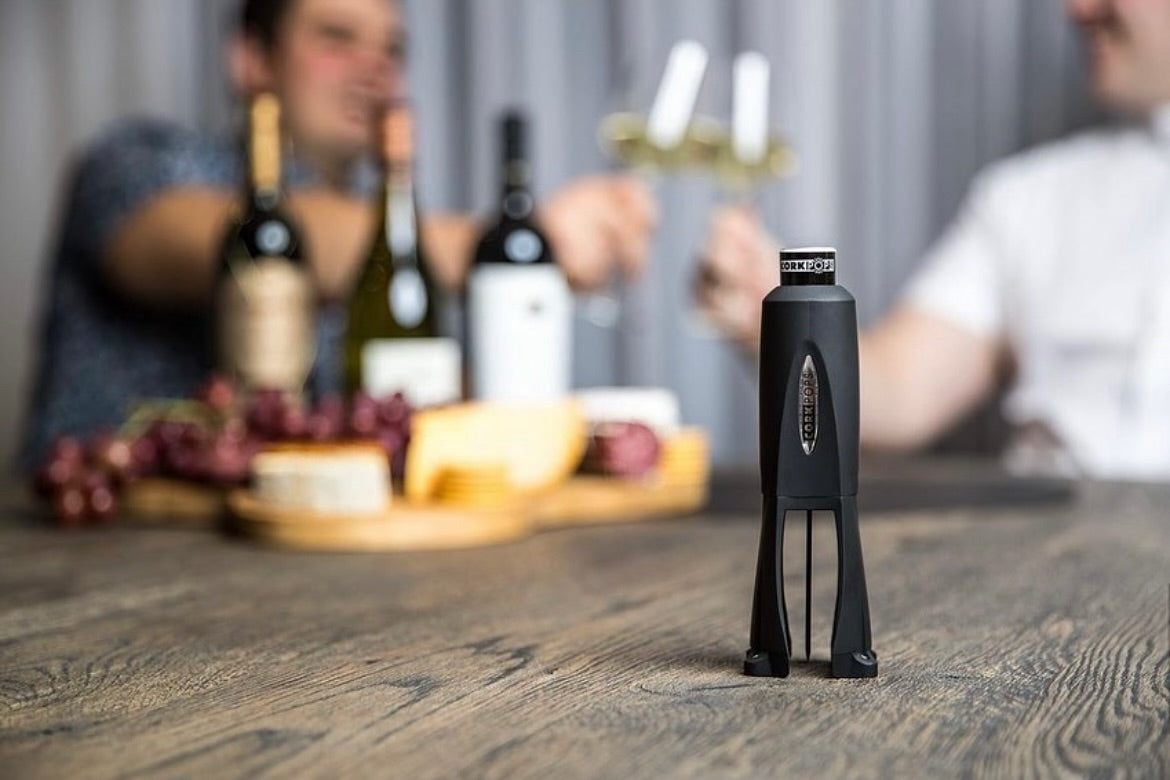 Cork Pops Legacy opener on a table with wine and cheese behind