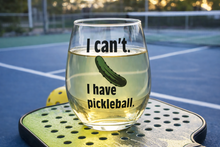 Wine glass on a green pickleball court surface beside a paddle