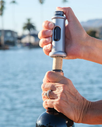Opening a bottle of wine with an Original Cork Pops opener beside the water